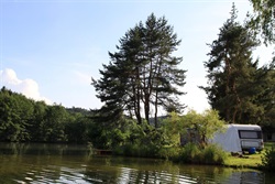 Caravan on the pond shore among trees
