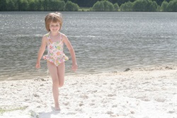 Little girl on the sandy beach by the pond